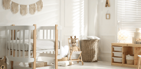A bright nursery with a white crib, wicker baskets, a stuffed deer toy, and natural wood furniture.