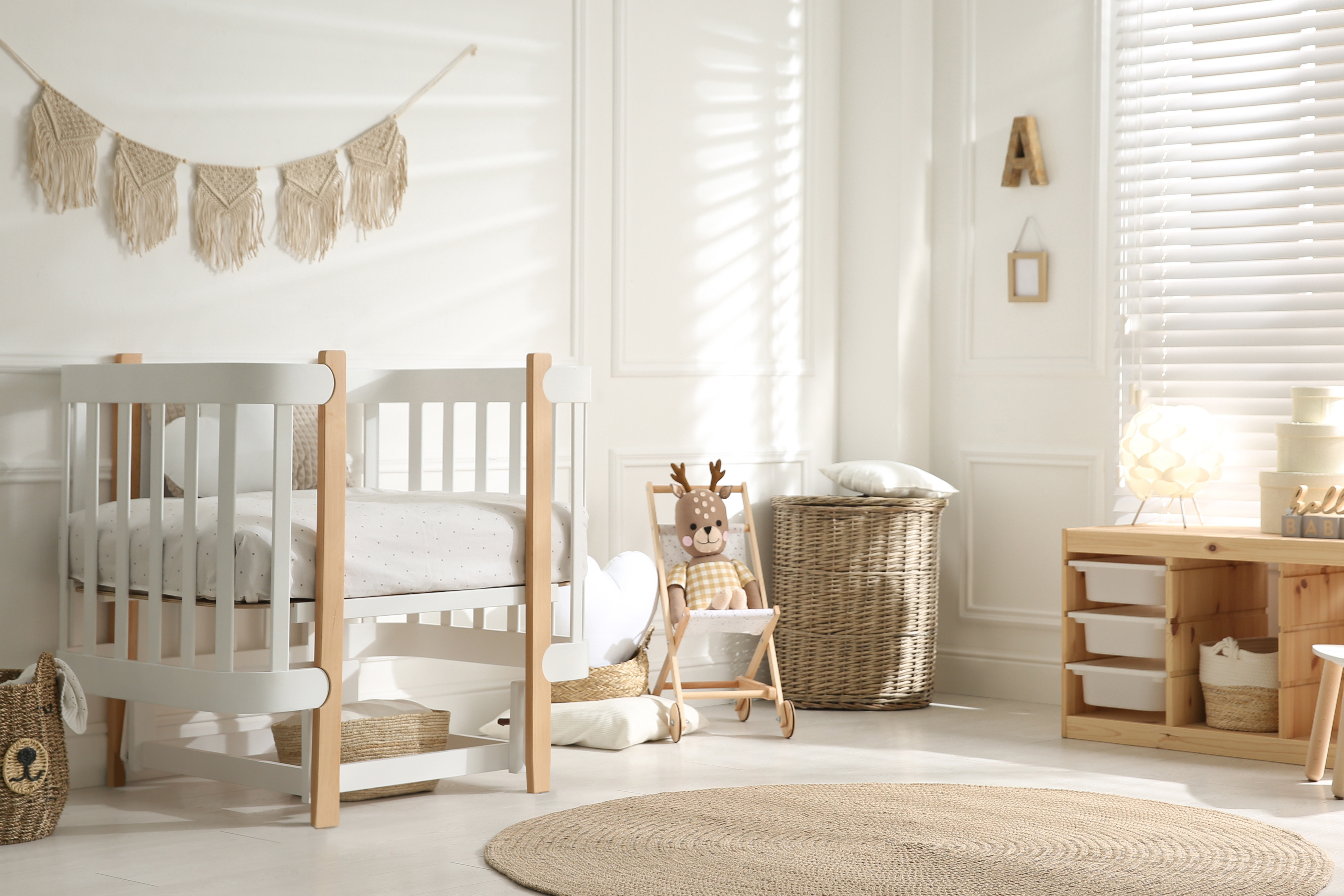 A bright nursery with a white crib, wicker baskets, a stuffed deer toy, and natural wood furniture.