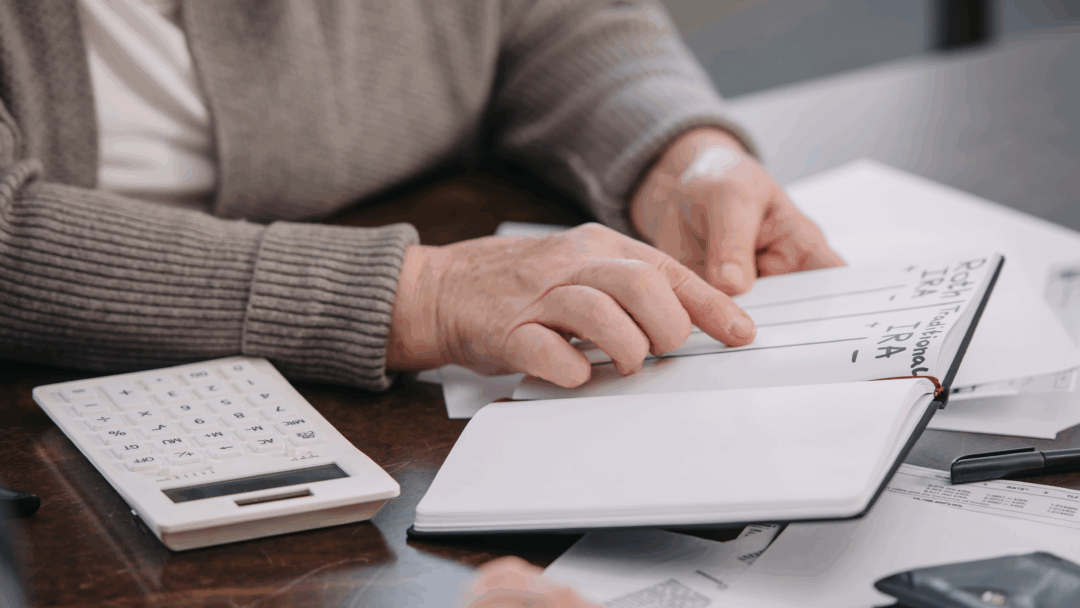 An older adult reviews notes about retirement accounts while going over financial paperwork at a table.