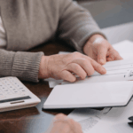An older adult reviews notes about retirement accounts while going over financial paperwork at a table.