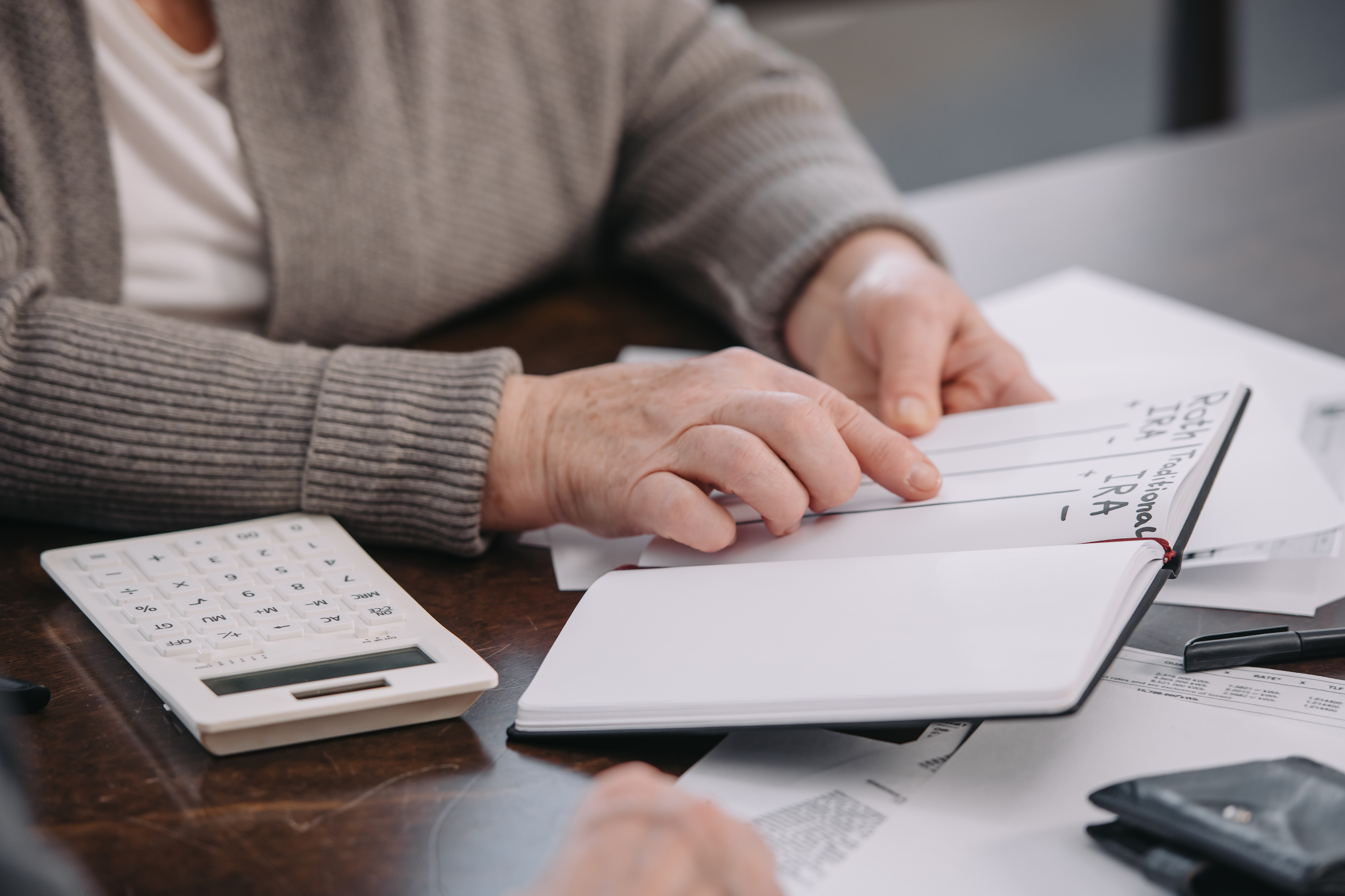 An older adult reviews notes about retirement accounts while going over financial paperwork at a table.