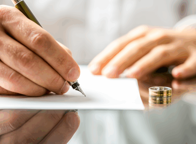 A person signs a document at a desk with a wedding ring placed beside the paper.