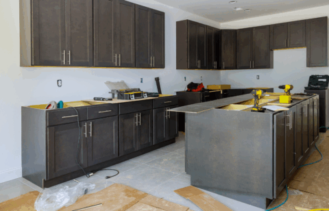 A kitchen under construction with dark cabinets, tools, and materials spread across the floor and counters.