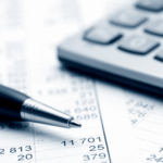 Close-up of a pen and calculator resting on financial documents with numbers.