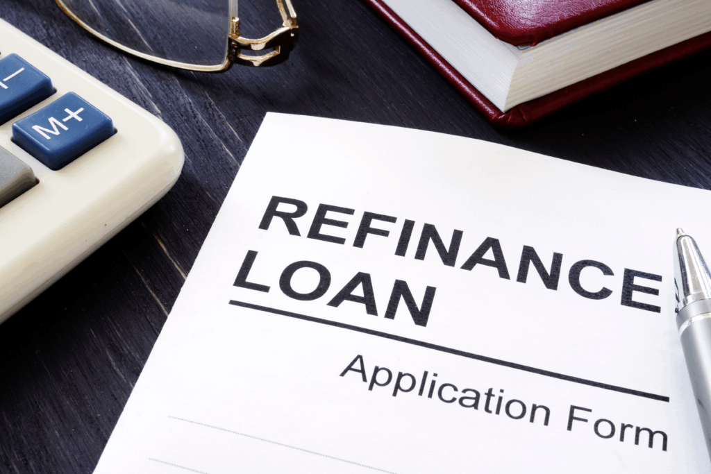 A refinance loan application form on a desk beside a calculator, glasses, and a pen.