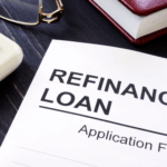 A refinance loan application form on a desk beside a calculator, glasses, and a pen.