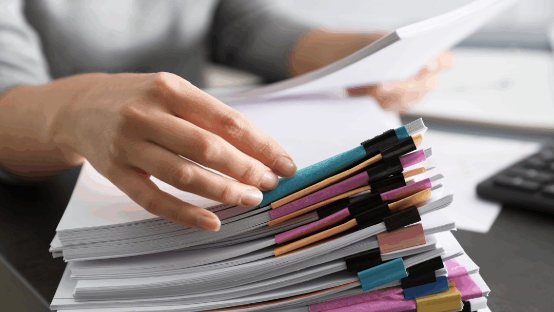 Hand organizing a large stack of documents secured with colorful binder clips on a desk.