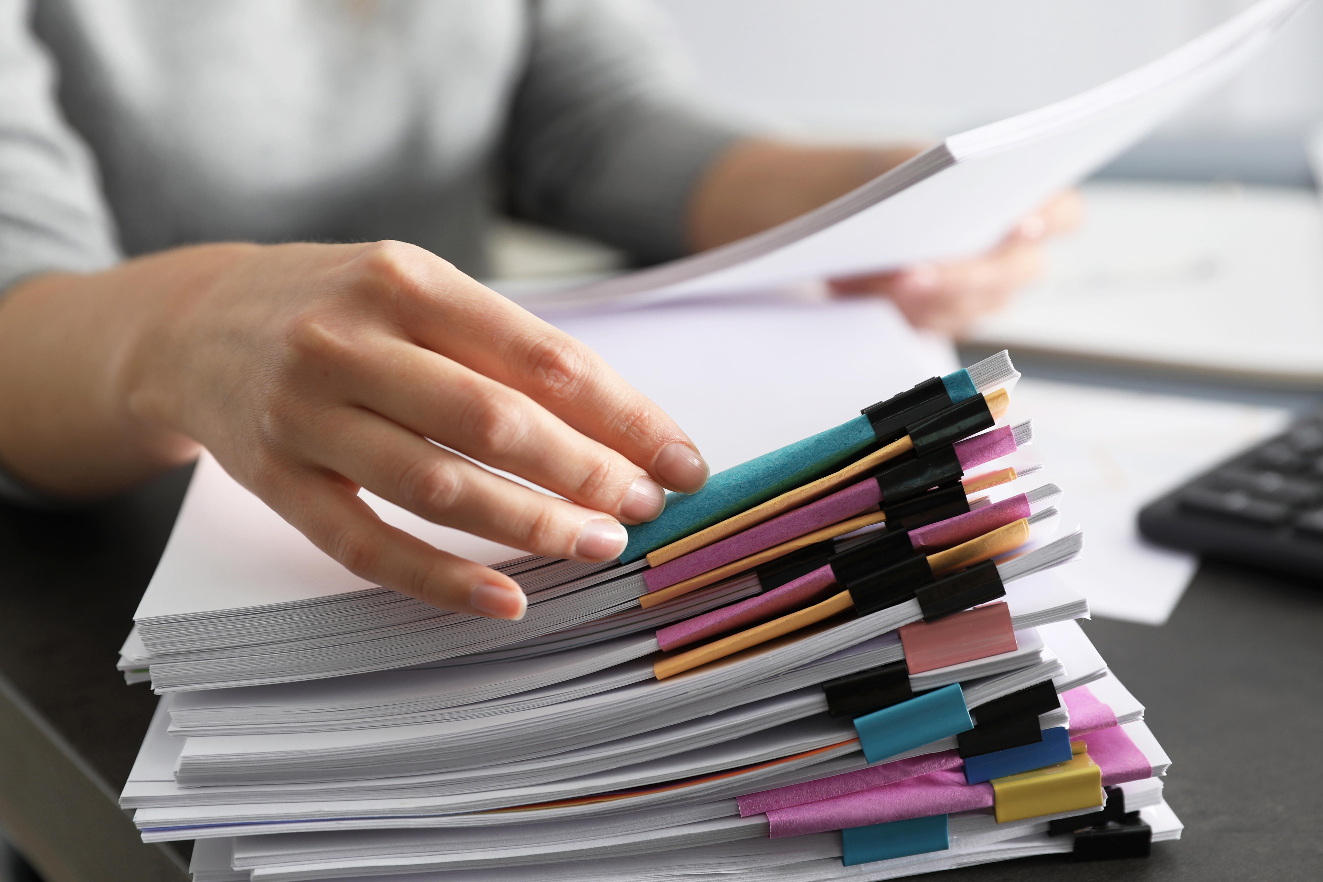 Hand organizing a large stack of documents secured with colorful binder clips on a desk.