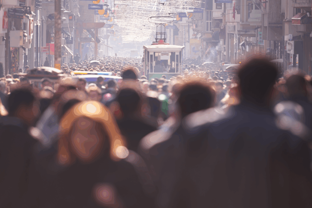 Large crowd of people walking along a busy city street with a streetcar visible in the distance.