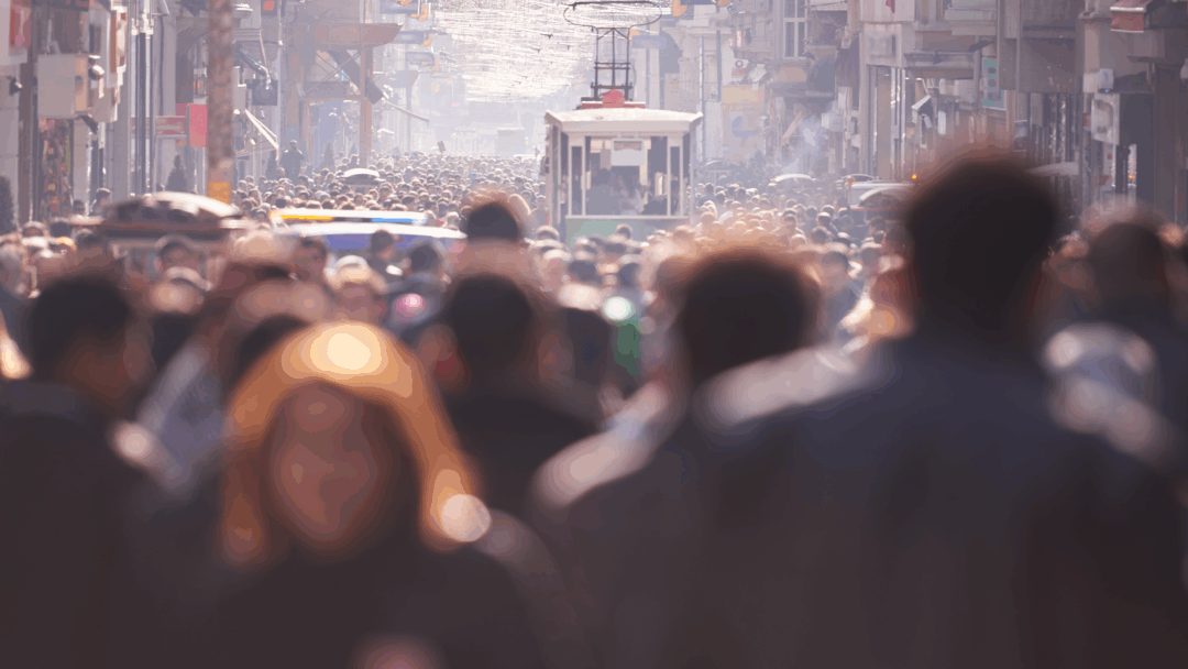 Large crowd of people walking along a busy city street with a streetcar visible in the distance.