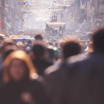 Large crowd of people walking along a busy city street with a streetcar visible in the distance.