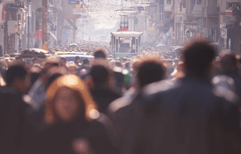 Large crowd of people walking along a busy city street with a streetcar visible in the distance.