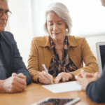 An older couple sits at a table with a professional, as one person signs a document while the others look on.