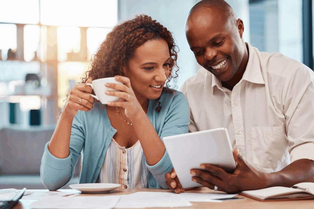 Couple sitting at a table reviewing financial documents on a tablet while drinking coffee at home.