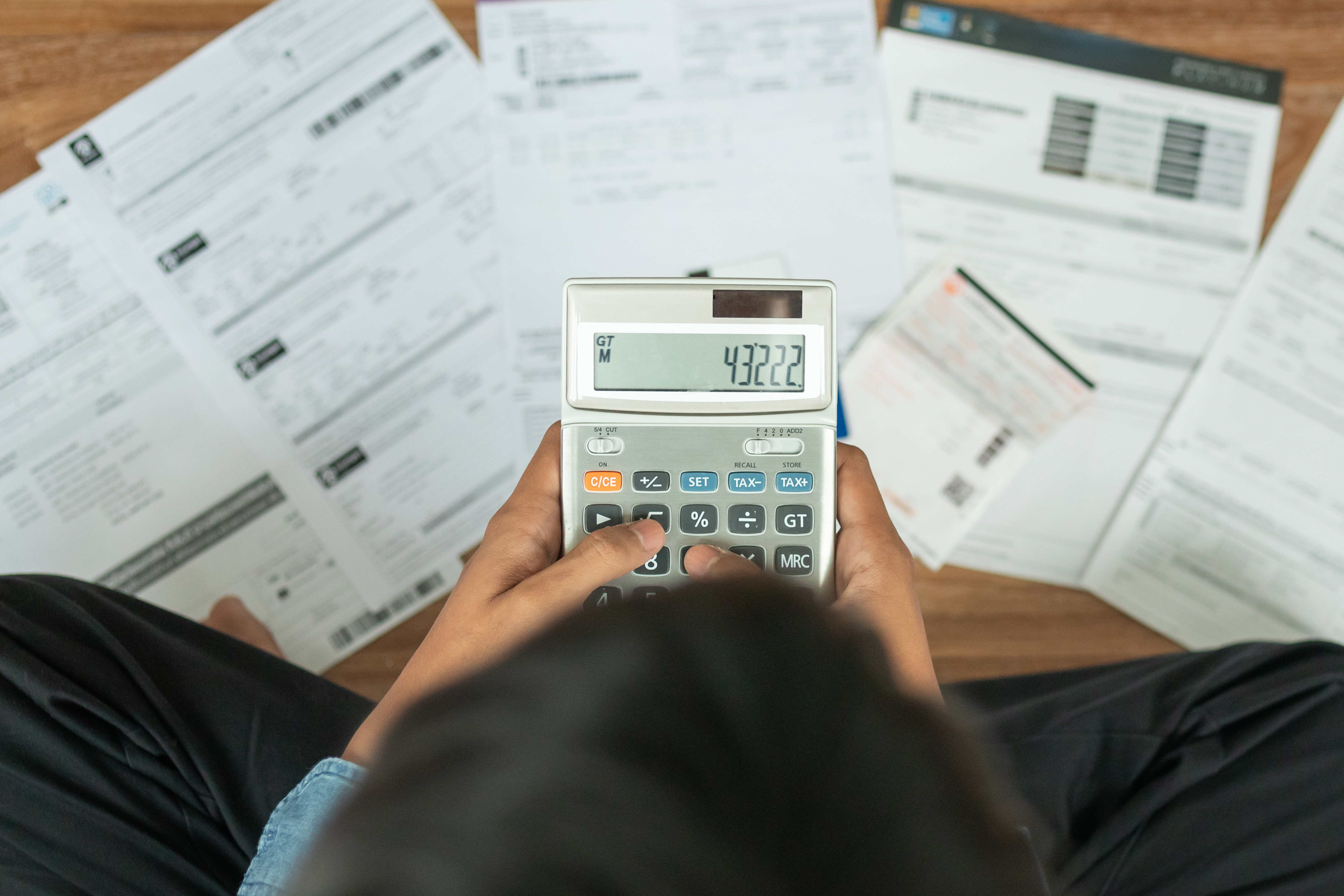 Person using a calculator while reviewing bills and financial documents spread across a desk.