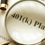 Magnifying glass highlighting the words “401(k) plan” on a printed document, with a calculator, pen, and cash nearby.