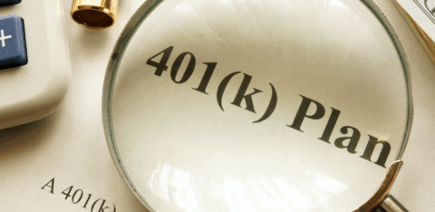 Magnifying glass highlighting the words “401(k) plan” on a printed document, with a calculator, pen, and cash nearby.
