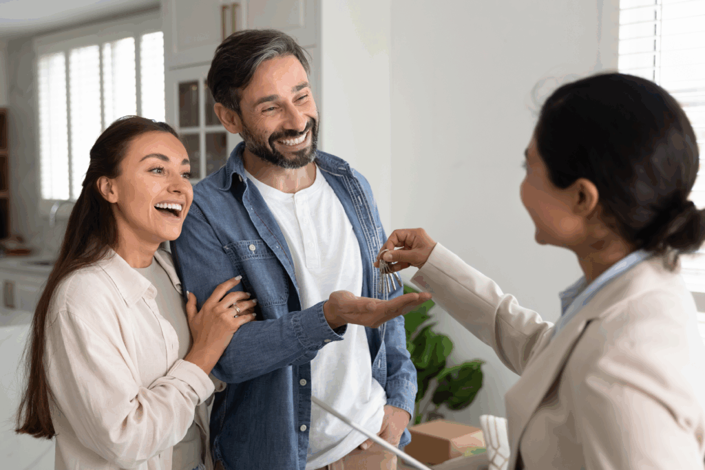 Real estate agent hands house keys to a smiling couple inside a new home.