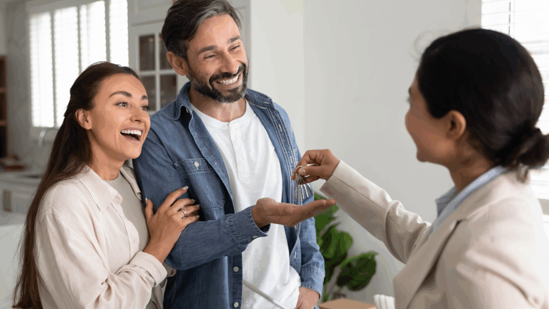 Real estate agent hands house keys to a smiling couple inside a new home.