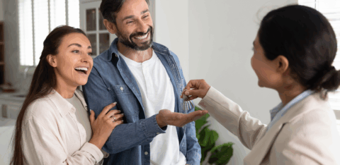 Real estate agent hands house keys to a smiling couple inside a new home.