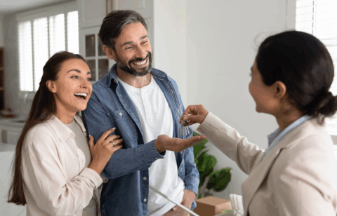 Real estate agent hands house keys to a smiling couple inside a new home.