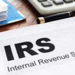 Close-up of paperwork labeled “IRS Internal Revenue Service” on a desk with a calculator and pen in the background.