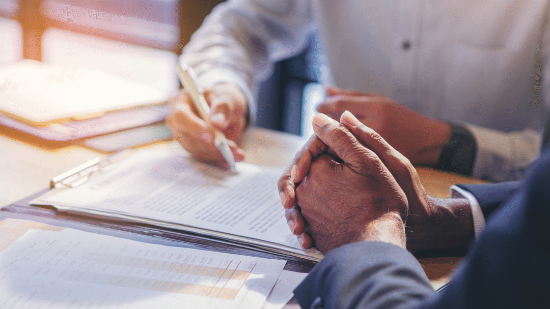 Close-up of two people reviewing and signing documents at a desk during a business meeting.