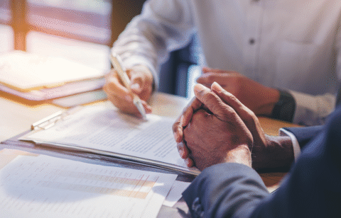 Close-up of two people reviewing and signing documents at a desk during a business meeting.