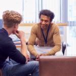 A professional meeting between two individuals in a small office, engaged in a focused and friendly conversation.
