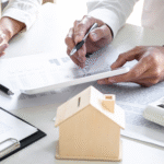 Two people reviewing financial documents with a calculator and small model house on the table.
