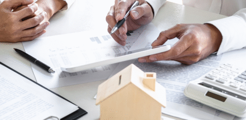 Two people reviewing financial documents with a calculator and small model house on the table.