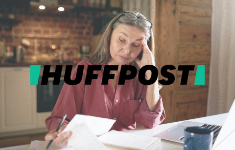 Older adult woman reviewing financial documents at home, appearing worried as she looks over papers next to an open laptop, with a HuffPost logo over the image.