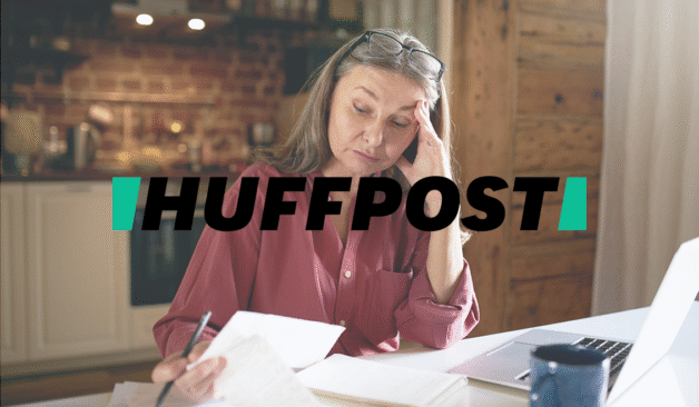 Older adult woman reviewing financial documents at home, appearing worried as she looks over papers next to an open laptop, with a HuffPost logo over the image.