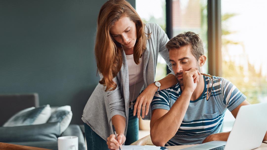 Couple reviewing financial documents at a table with a laptop and coffee mug.