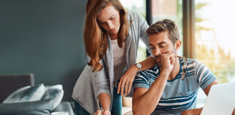Couple reviewing financial documents at a table with a laptop and coffee mug.