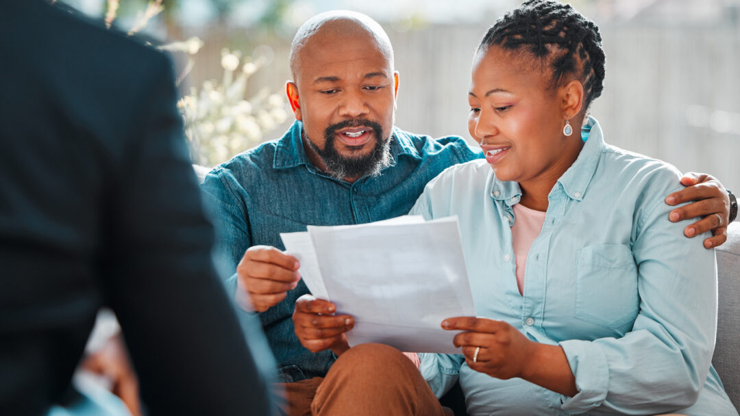 Couple sitting together and reviewing paperwork while speaking with a person across from them.