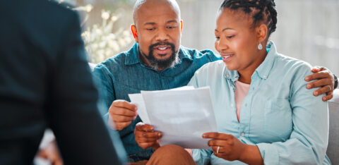 Couple sitting together and reviewing paperwork while speaking with a person across from them.