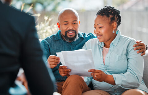 Couple sitting together and reviewing paperwork while speaking with a person across from them.