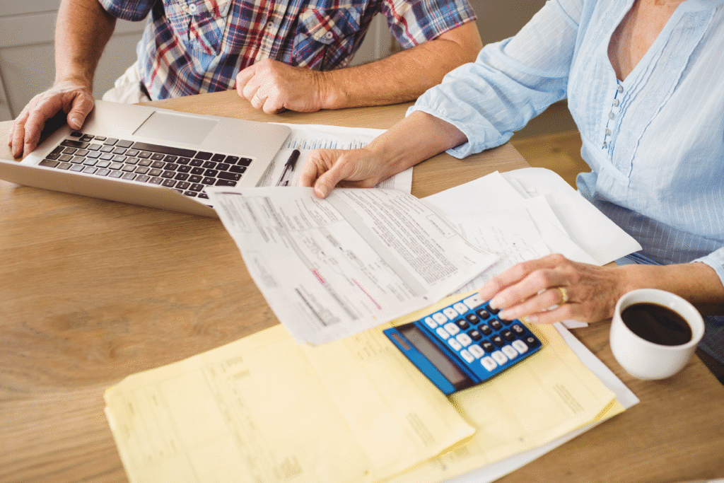 Couple reviewing financial paperwork at a table with a laptop, calculator, and coffee.