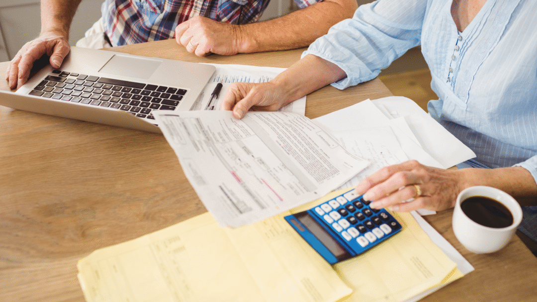 Couple reviewing financial paperwork at a table with a laptop, calculator, and coffee.