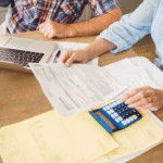 Couple reviewing financial paperwork at a table with a laptop, calculator, and coffee.