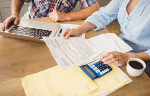 Couple reviewing financial paperwork at a table with a laptop, calculator, and coffee.