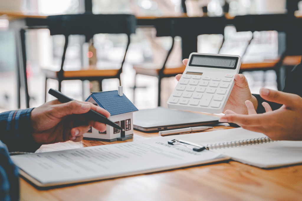 Two people reviewing financial documents with a calculator and small model house on the table.