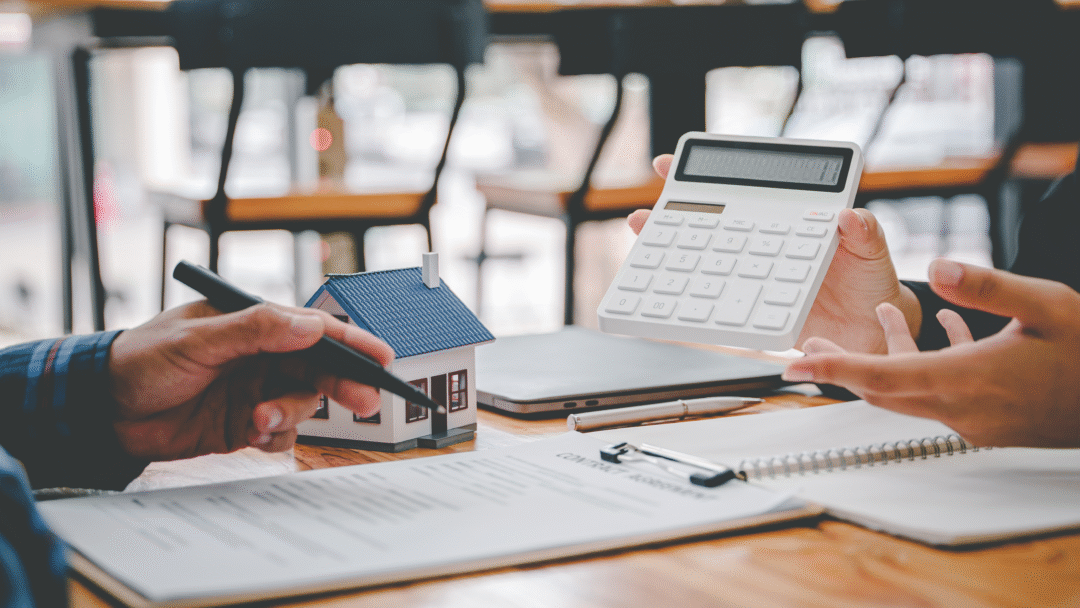 Two people reviewing financial documents with a calculator and small model house on the table.