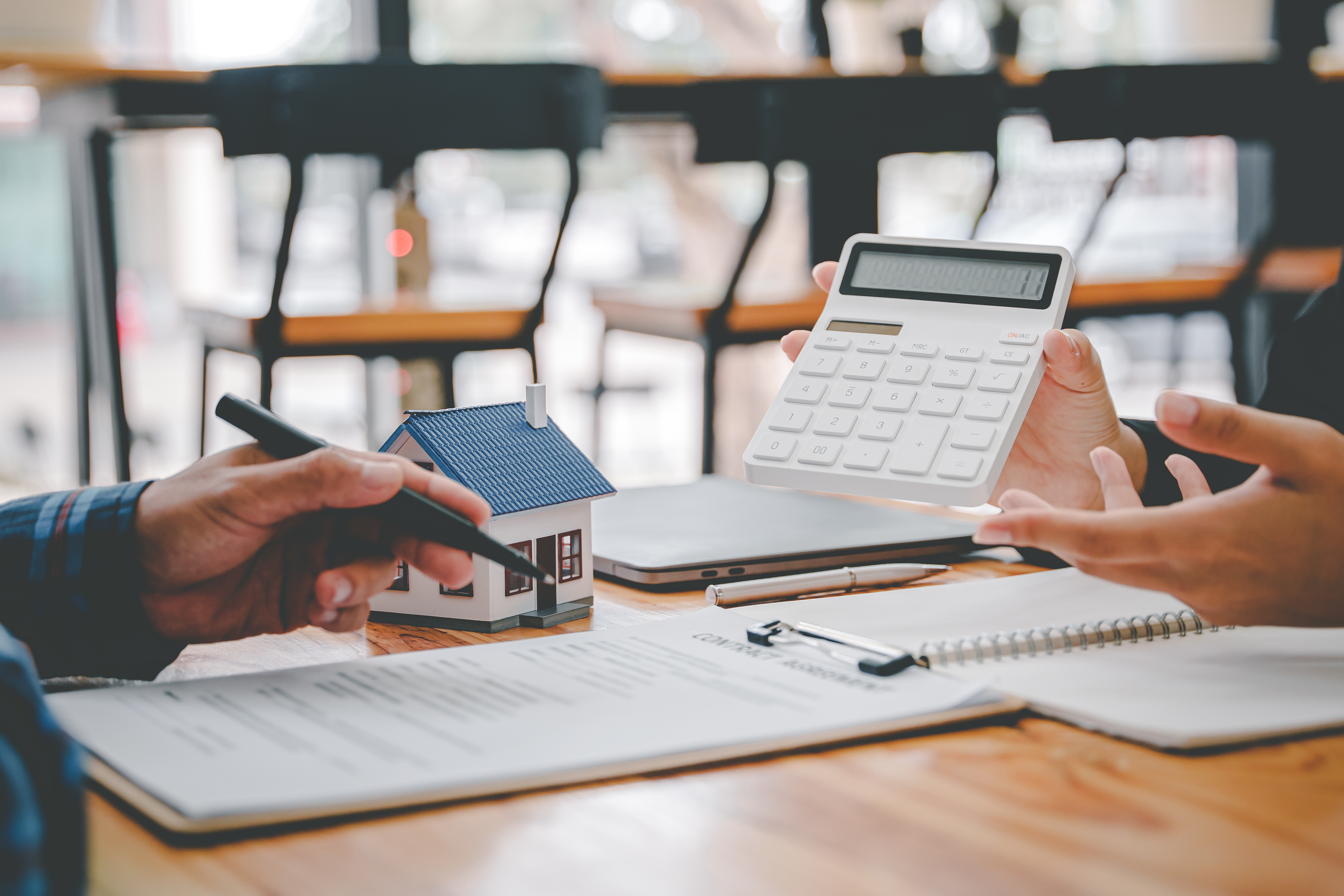 Two people reviewing financial documents with a calculator and small model house on the table.