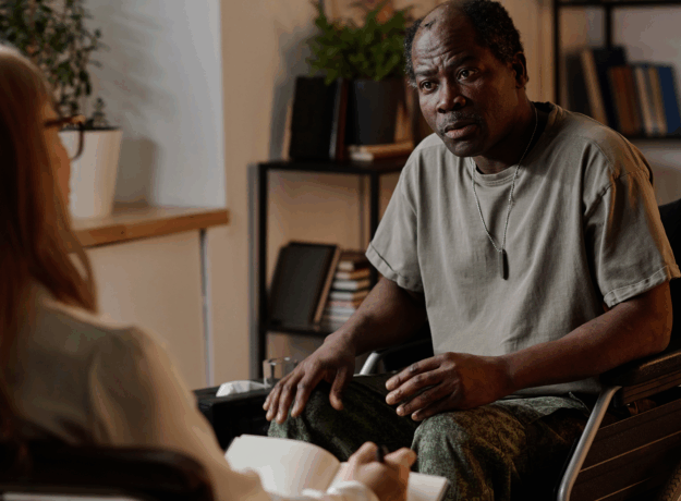 Man in a wheelchair speaking with another person during a seated conversation in an office setting.