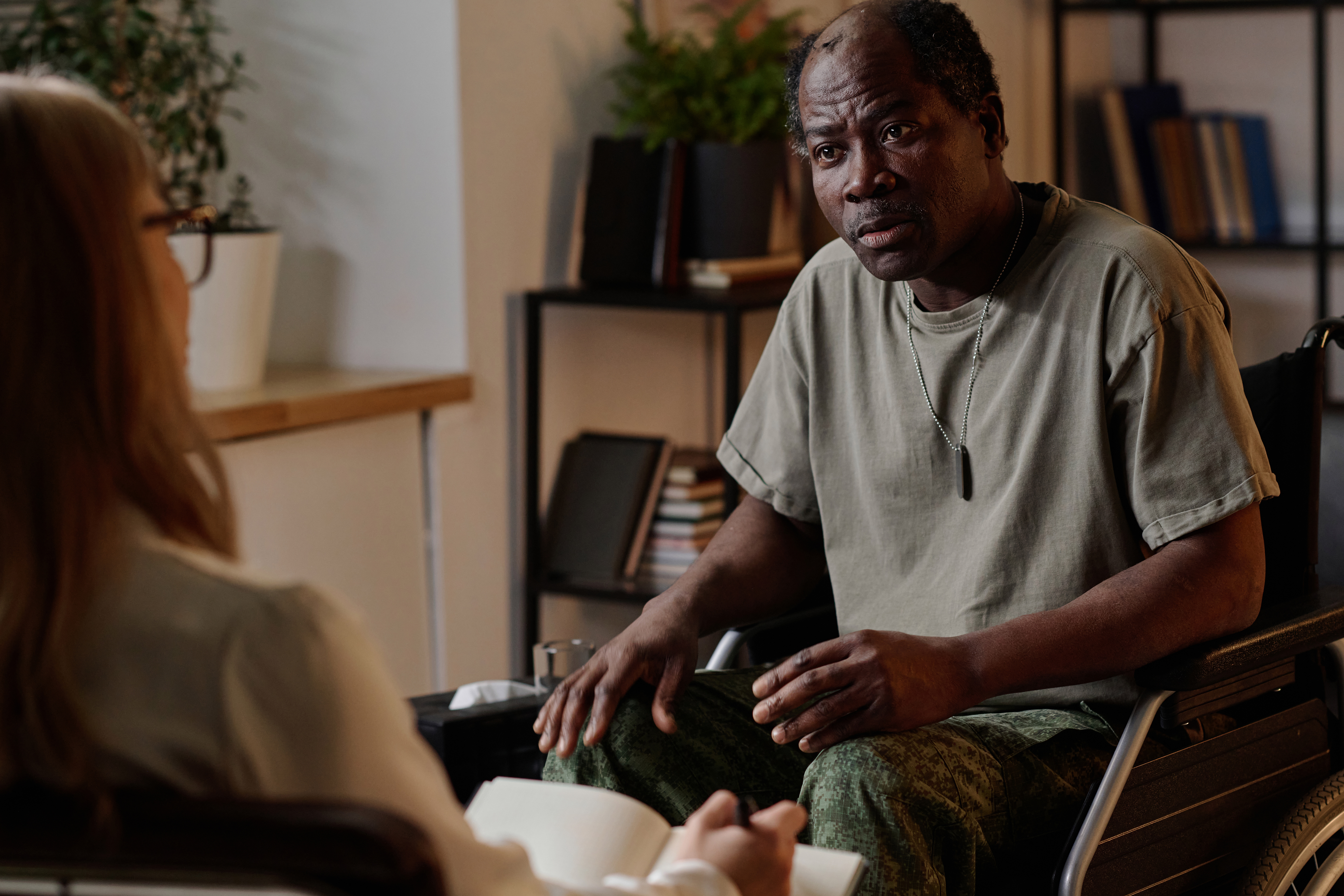 Man in a wheelchair speaking with another person during a seated conversation in an office setting.
