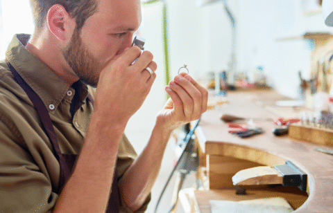 Man inspecting a ring closely using a jeweler’s loupe in a jewelry workshop.