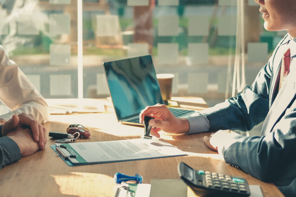 Person stamping a document at a desk with car keys, a calculator, and a laptop nearby.