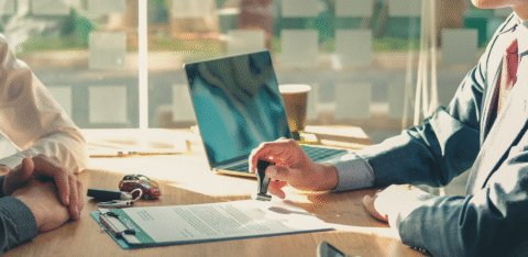 Person stamping a document at a desk with car keys, a calculator, and a laptop nearby.